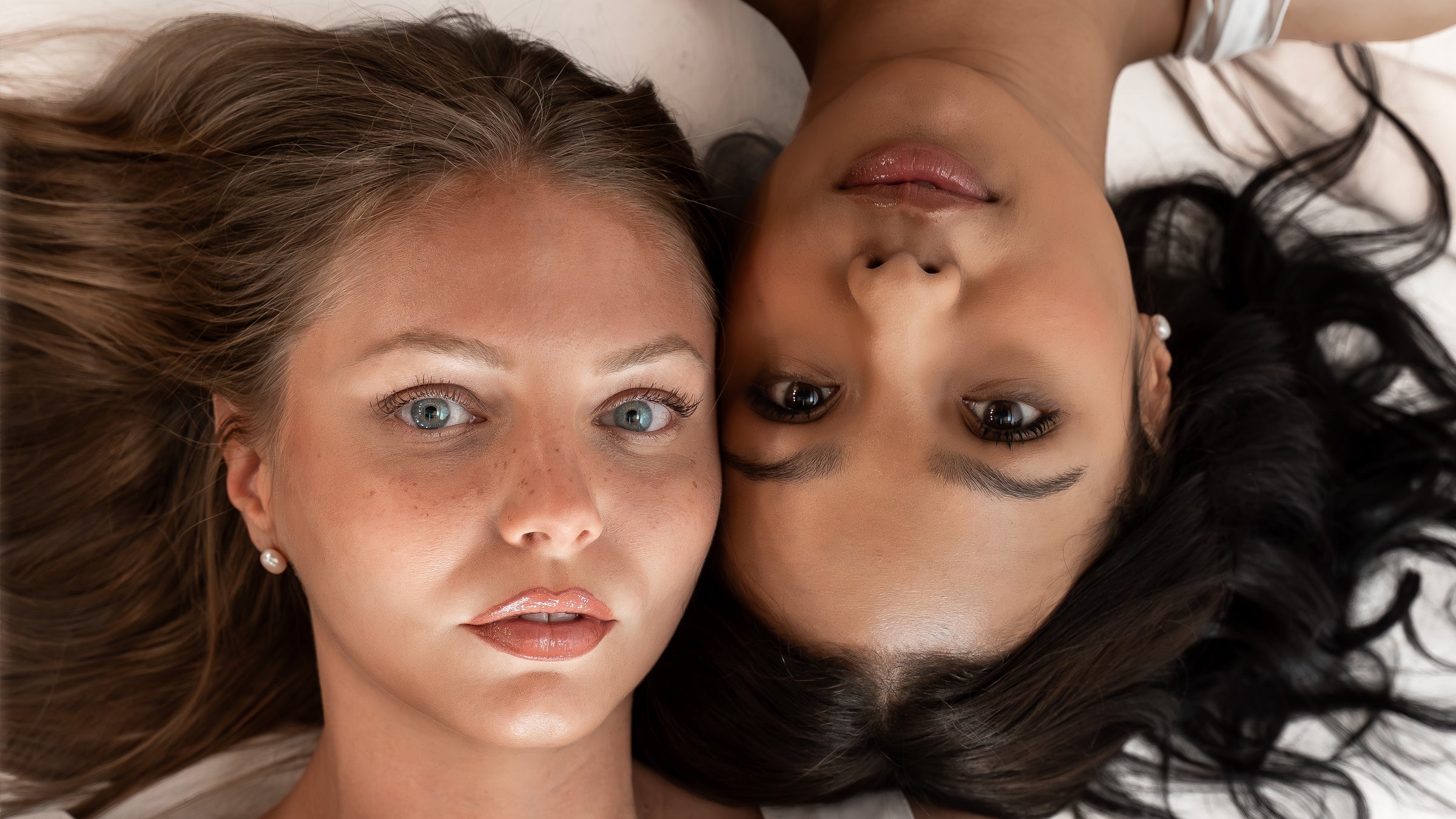 Two women lying down with their heads close together, facing the camera.