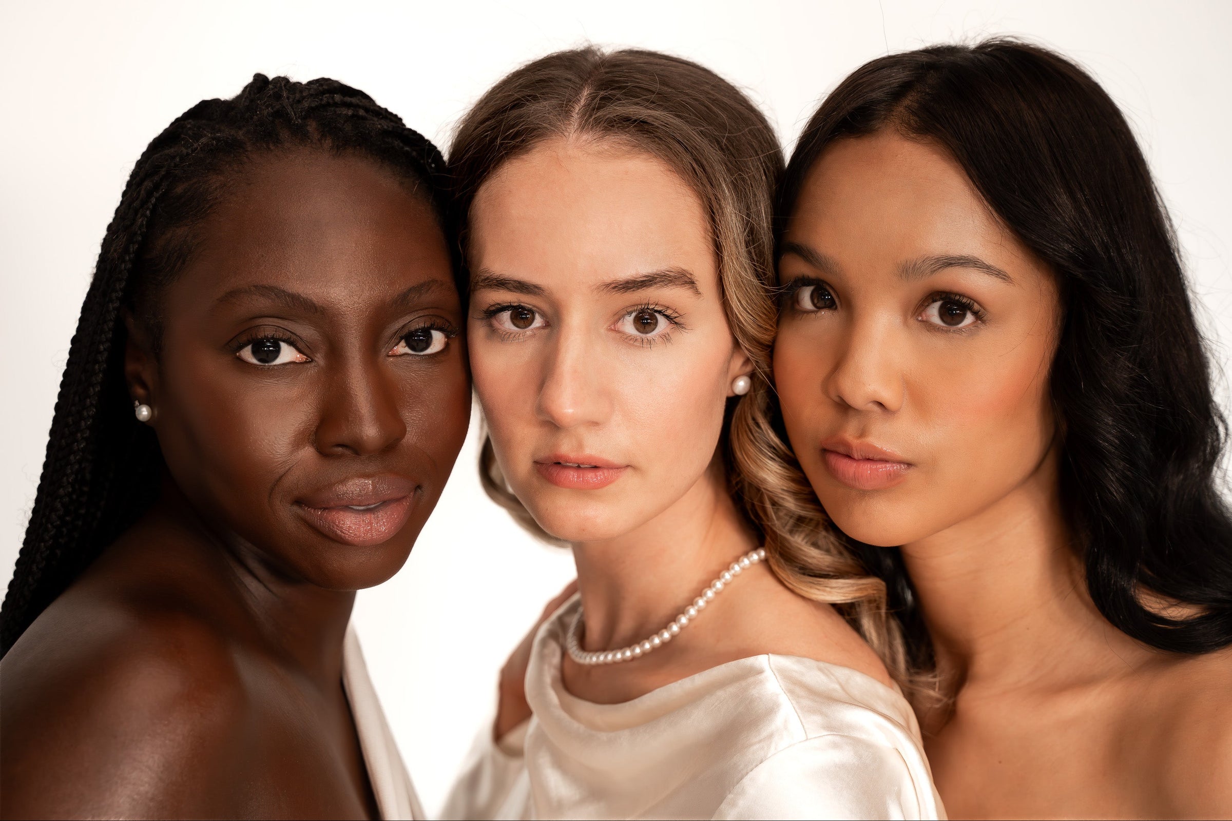 Three women of different ethnicities standing close together against a white background