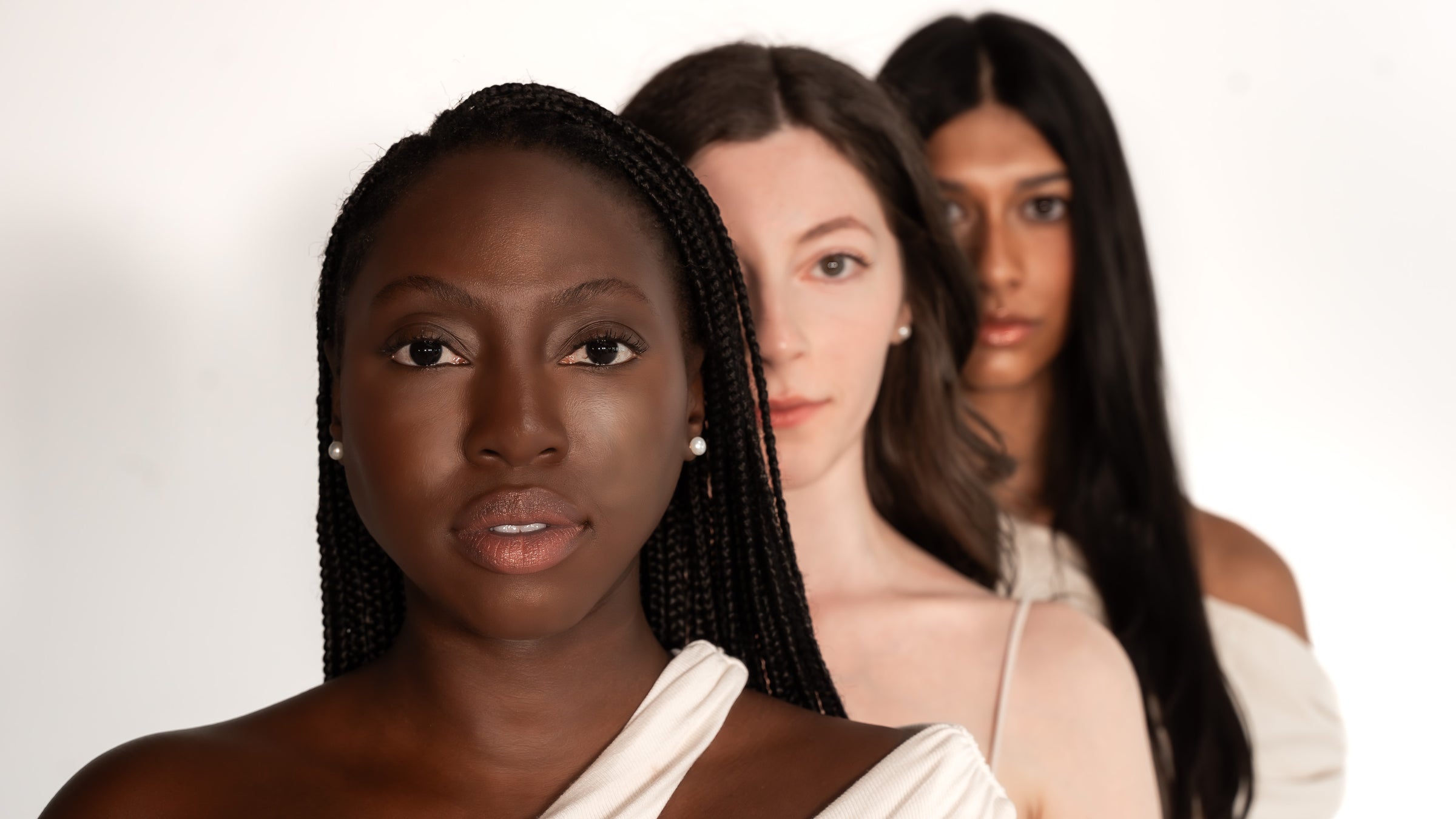Three women with different hair styles and skin tones standing close together on a white background