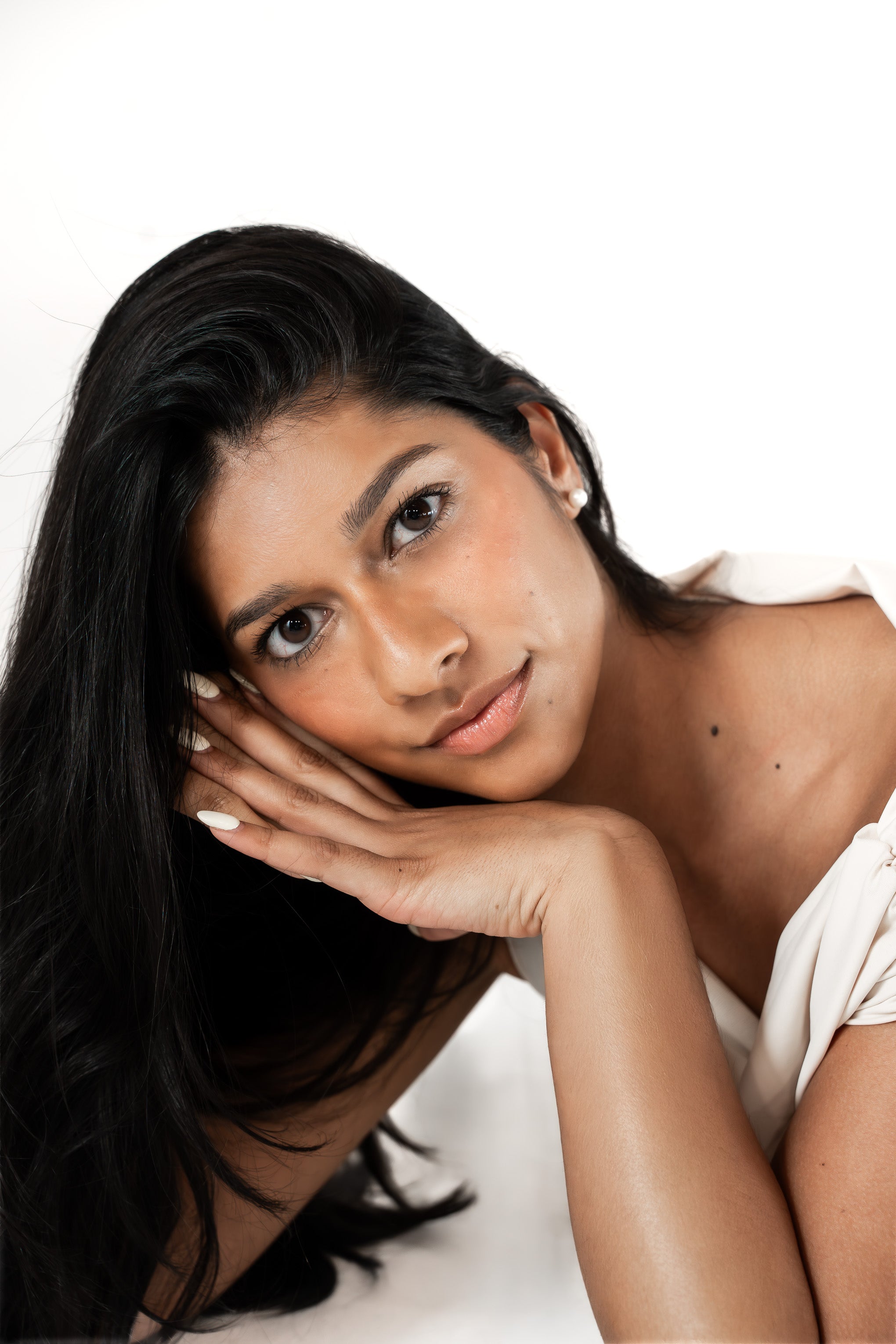 Woman with dark hair resting her head on her hand against a white background