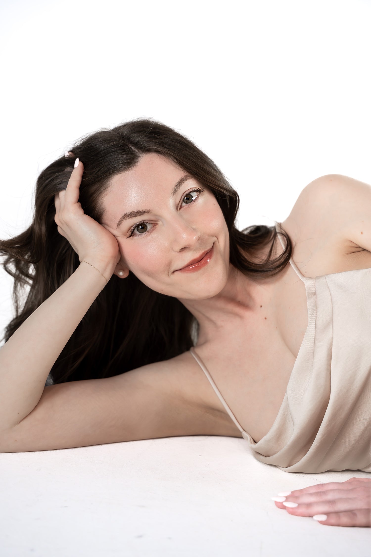 Woman in a beige dress lying on a white surface with a plain background